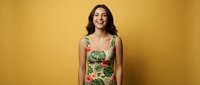 Young Hispanic woman in tropical print dress smiling confidently against warm yellow background for fashion and lifestyle content.