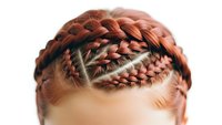Close-up of intricate braided hairstyle with multiple plaits and geometric parting on woman's head showing detailed hair texture and styling technique.