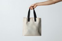 Female hand holding minimal beige canvas tote bag with black handles against white background, mockup for eco-friendly shopping and branding design.