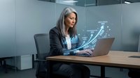 Professional Asian businesswoman analyzing financial growth data on laptop with holographic chart projection showing upward trend in modern office environment.