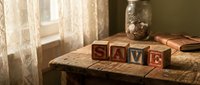 Vintage wooden alphabet blocks spelling LOVE on rustic table with warm sunlight streaming through lace curtains creating nostalgic home decor atmosphere.