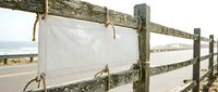 White fabric banners hanging on rustic wooden fence posts with rope ties, coastal farmhouse decor for outdoor events and rustic wedding ceremonies.