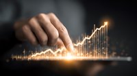 Hand touching glowing financial chart on digital tablet screen, rising trend line showing business growth and success in dark background.