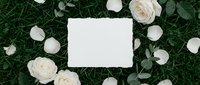 Blank white card surrounded by cream roses and eucalyptus on green grass background for wedding invitations, greeting cards and romantic designs.