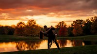 Romantic couple silhouette dancing by lake at golden sunset with dramatic orange sky and autumn trees reflecting in calm water for wedding concepts.