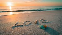 Word Love handwritten in wet sand on a tropical beach at golden sunset, with a heart-shaped stone, romantic seaside scene.