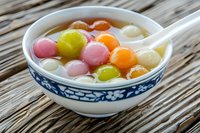 Colorful glutinous rice balls tang yuan in sweet soup served in traditional ceramic bowl on bamboo mat for Chinese dessert celebration.