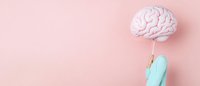 Pink brain model held by hand in medical glove against pastel pink background, creative minimal healthcare composition with copy space for text.