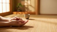 Peaceful meditation hands resting on bamboo mat in warm sunlit room with traditional tea bowl creating serene mindfulness atmosphere for wellness practice.