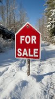 Red for sale sign in snowy winter landscape with bare trees and evergreens under clear blue sky for real estate marketing and property advertisements.