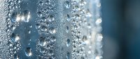 Close-up macro shot of crystal clear water droplets and bubbles on transparent glass surface with soft blue background for refreshing concepts.
