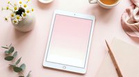 White tablet with blank pink screen on feminine workspace with flowers, tea cup and rose gold accessories for mockup design projects.