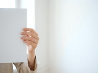 Woman holding blank white card or sign with manicured hand, wearing beige sleeve against bright white background for advertising and promotional messaging.