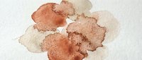 Abstract watercolor stains in warm earth tones creating organic flowing shapes on textured paper background for artistic design projects.