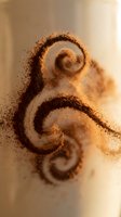 Swirling brown powder particles forming decorative spiral patterns against neutral background, suitable for abstract design, texture overlays, and creative visual effects.