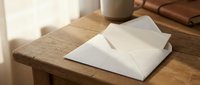 White envelope on rustic wooden desk with warm sunlight streaming through window creating peaceful morning workspace atmosphere for correspondence.