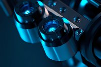 Macro shot of modern microscope lenses with blue illumination showing precision optical equipment details and scientific research instruments in dark setting.