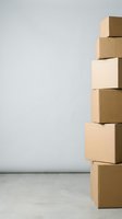 Stacked cardboard boxes in various shades arranged vertically against white wall with concrete floor, representing shipping, logistics, storage, and delivery services for business and commerce.