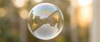 Single soap bubble floating in air with rainbow iridescent surface reflecting warm sunlight and blurred bokeh background for dreamy atmospheric concepts.