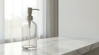 Clear glass soap dispenser on white marble countertop in bright modern bathroom with natural window light for hygiene and home decor concepts.