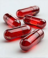Red transparent capsules with liquid medicine on white background, macro photography showing pharmaceutical details and reflective surfaces.