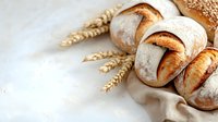 Freshly baked artisan bread rolls with crispy golden crust on linen cloth, accompanied by wheat ears on light background.