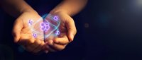 Cupped hands holding glowing atomic structure with orbiting electrons against dark background. Science education and molecular physics concept.