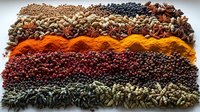 Colorful rows of aromatic spices and seasonings arranged in vibrant stripes pattern including turmeric, peppercorns, cardamom, star anise, and various dried herbs.