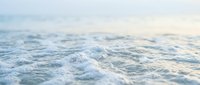 Soft ocean waves with white foam rolling onto sandy shore at sunrise or sunset, suitable for travel, wellness, and coastal lifestyle marketing.