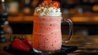 Fresh strawberry smoothie with whipped cream and berry garnish in glass mug on wooden table. Healthy breakfast drink for cafe menu and recipe content.