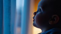 Young Caucasian boy looking up through window at night, illuminated by moonlight, profile silhouette against blue tinted glass, wearing casual clothing, dreamy atmospheric mood.