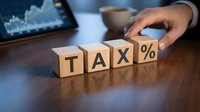 Businessman hand arranging wooden blocks spelling tax percent symbol at desk with financial charts, representing tax planning, accounting, and financial management strategy.