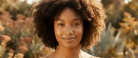 Young African American woman with natural curly afro hair smiling warmly in golden hour sunlight with soft bokeh background for lifestyle and beauty content.