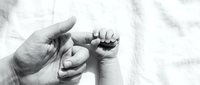 Tender moment of adult hand gently holding tiny newborn baby foot in black and white photography capturing precious early bonding between parent and child.