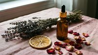 Amber dropper bottle with lavender bunch, dried rose petals, and citrus slice on pink linen, natural aromatherapy and skincare concept.