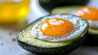 Baked egg in fresh avocado half sprinkled with black pepper and seasonings, close up view showing runny yolk and creamy texture. Healthy breakfast concept.
