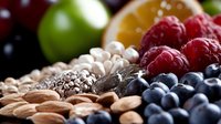 Fresh organic berries, nuts and seeds arranged in rows on dark background, selective focus on ripe raspberries and blueberries with almonds and chia seeds.