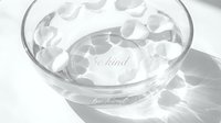 Glass bowl with water and floating white rose petals, engraved with be kind text, soft shadows, monochrome spa wellness aesthetic.