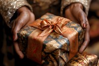Elegant gift box wrapped in vintage floral pattern paper with copper satin ribbon bow, held by hands in festive celebration moment. Perfect for holiday designs.