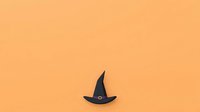 Isolated black witch hat with buckle on warm peach background, ready for Halloween designs, invitations, and seasonal marketing materials.