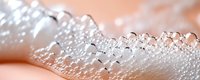 Macro photography of water droplets forming delicate line pattern on soft pink surface, creating natural geometric shapes with light refraction and bokeh effect.