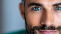 Close up portrait of a bearded man with striking blue eyes and gentle smile against blurred background, suitable for wellness, lifestyle and beauty concepts.