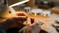 Skilled jeweler hands crafting delicate ring at workbench with professional tools and warm lighting in artisan workshop for custom jewelry making and repair.