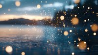 Magical winter scene with glowing bokeh lights and snowflakes falling over frozen lake surface at sunset, mountains silhouette in background creates dreamy atmosphere.