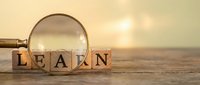 Wooden blocks spelling LEARN with a magnifying glass on a rustic table, warm golden background symbolizing education and knowledge discovery.