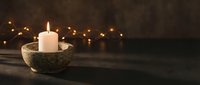 Burning white candle in stone bowl with warm bokeh lights creating cozy atmospheric mood for relaxation meditation spa wellness and home decor concepts.