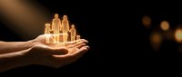 Hands holding glowing family figures representing protection, care and insurance concept on dark background with warm bokeh lights.