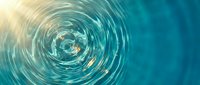 Circular ripples spreading across turquoise water surface with golden sunlight reflection creating concentric wave patterns in calm liquid.