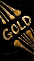 Gold makeup brushes with natural bristles arranged around gold lettering on black marble background, perfect for beauty and cosmetics design projects.