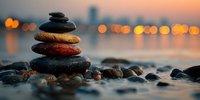 Balanced stone cairn on beach at sunset with city lights bokeh in background, symbolizing meditation and wellness.
